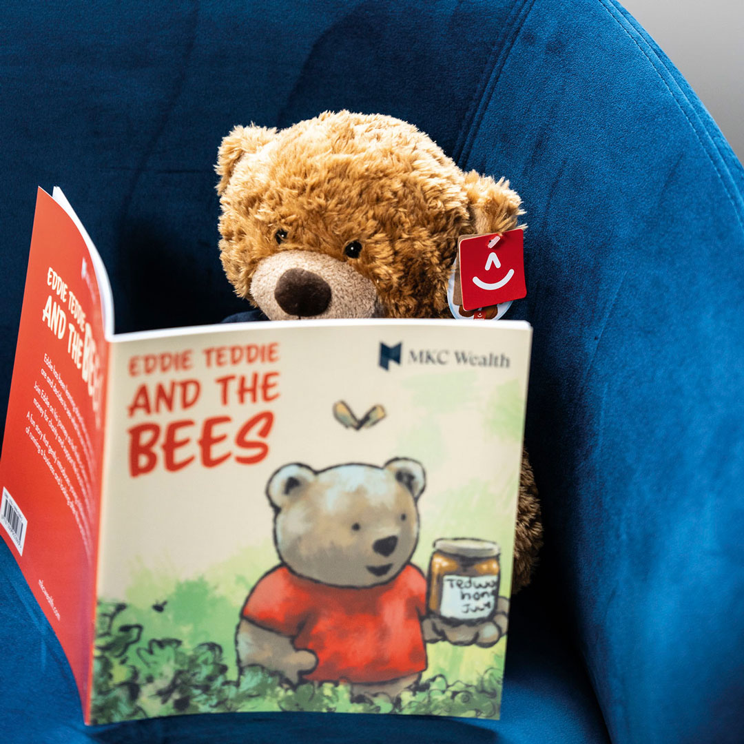 Plush toy of MKC Wealth's Eddie Teddie reading 'Eddie Teddie and The Bees', promoting children's financial literacy.