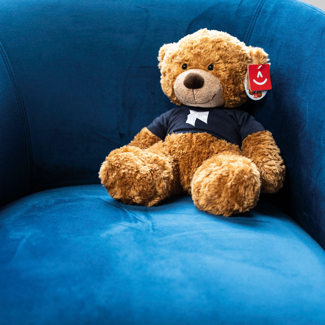 Plush toy of MKC Wealth's Children's Financial Coach, Eddie Teddie, sitting on a chair.